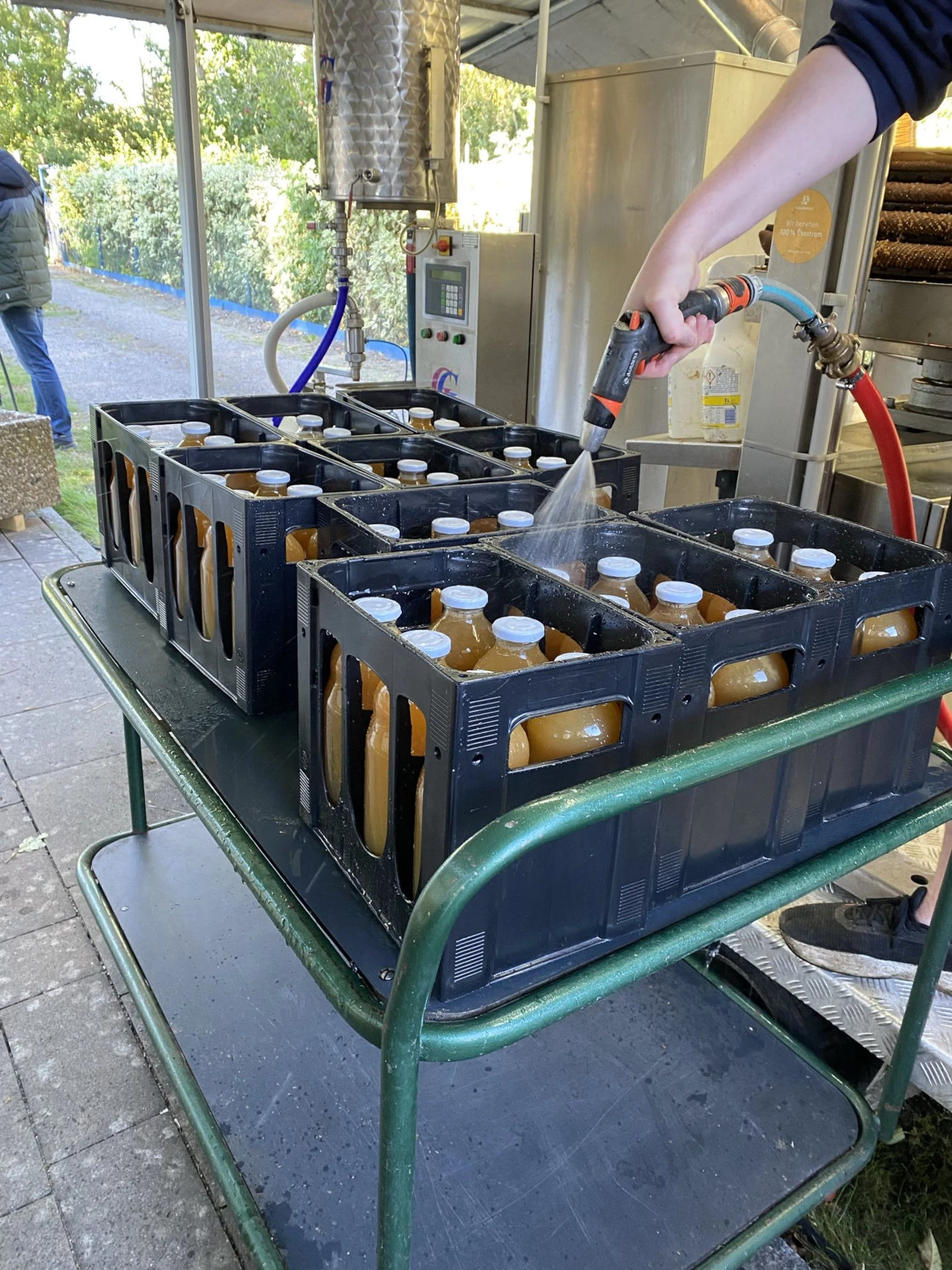 10 Saftkisten mit jeweils 6 Flaschen Apfelsaft stehen auf einem Tisch und werden mit einem Wasserschlauch gereinigt.